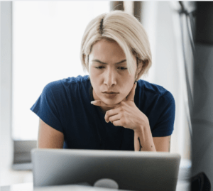 Person leaning over a laptop with a concerned, thoughtful expression while reviewing something online